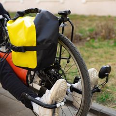Yellow and black roll-top pannier on the rear rack of a recumbent bike, the rider's white trainers on the pedals