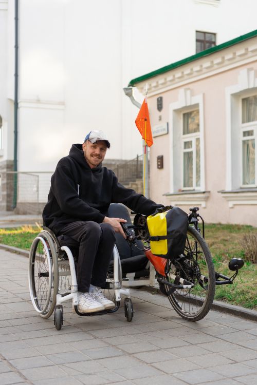 Free A smiling man in a wheelchair with a bicycle on a pavement outdoors. Stock Photo