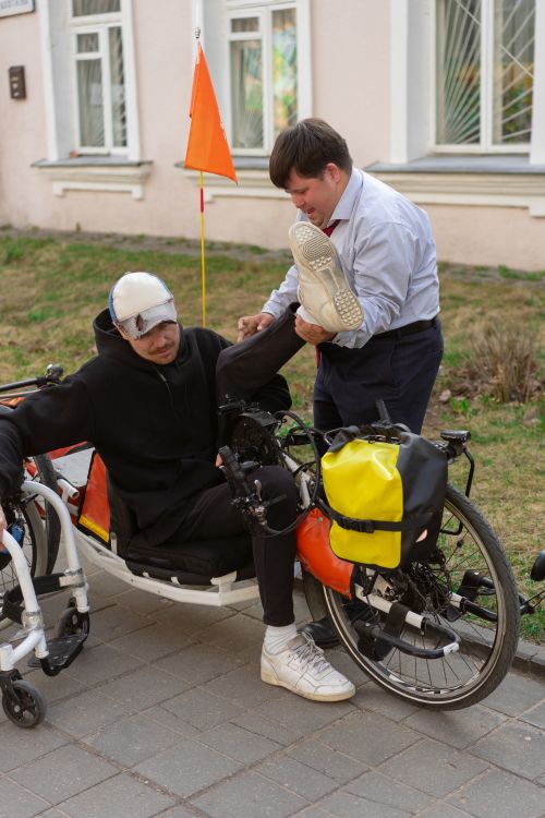 Free A man helps a cyclist with a mobility aid adjust on an urban street. Stock Photo