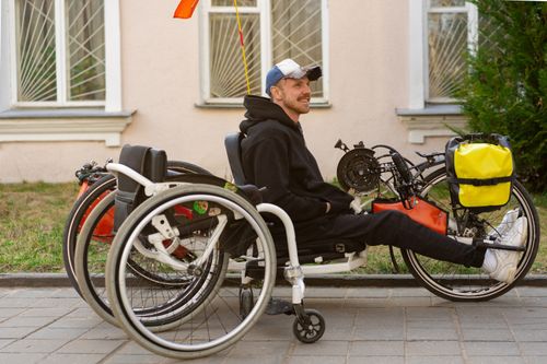 Free Man in a black hoodie sits smiling on a handcycle in an outdoor urban setting. Stock Photo