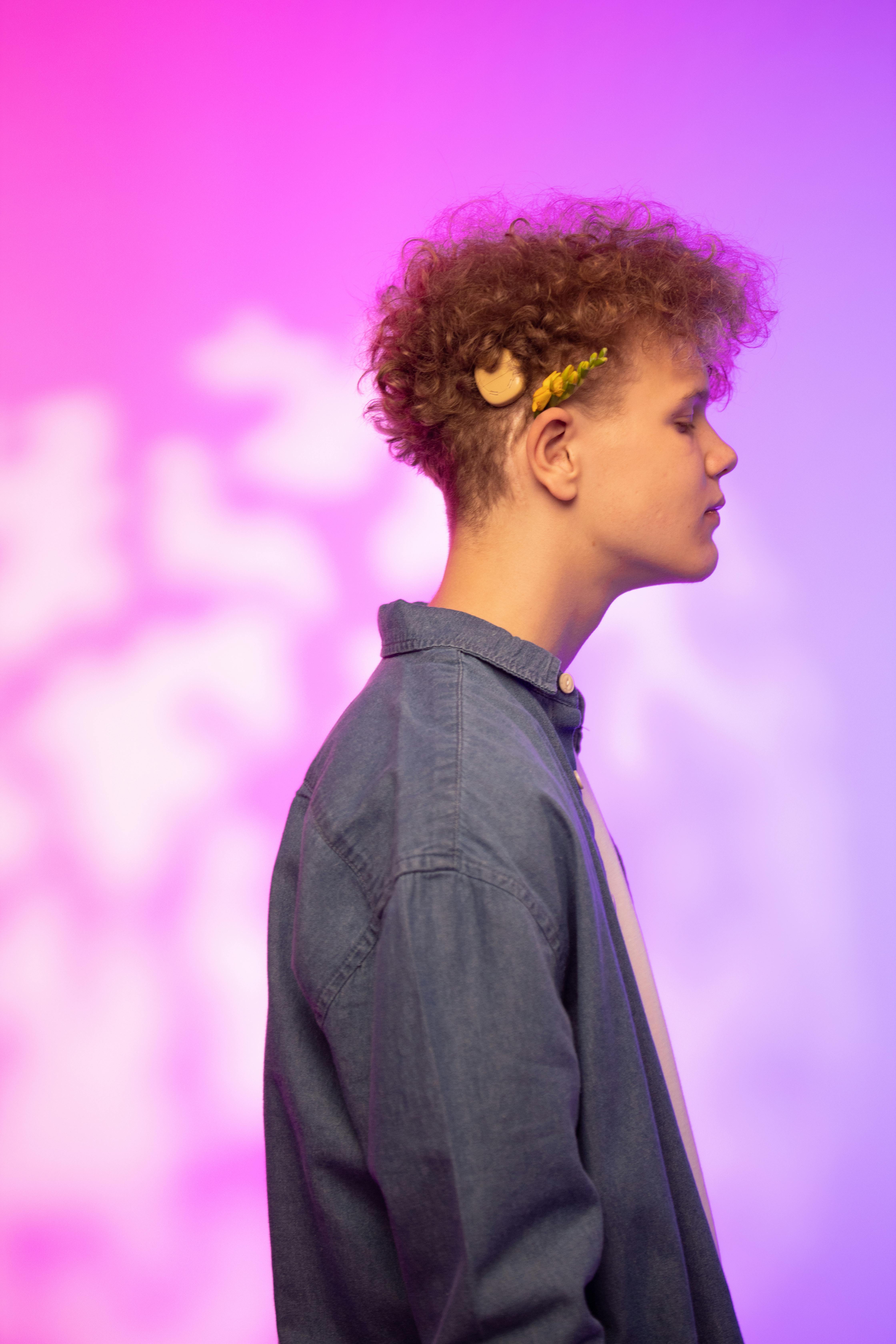 Profile shot of a young man with curly hair against a pink and purple gradient backdrop.