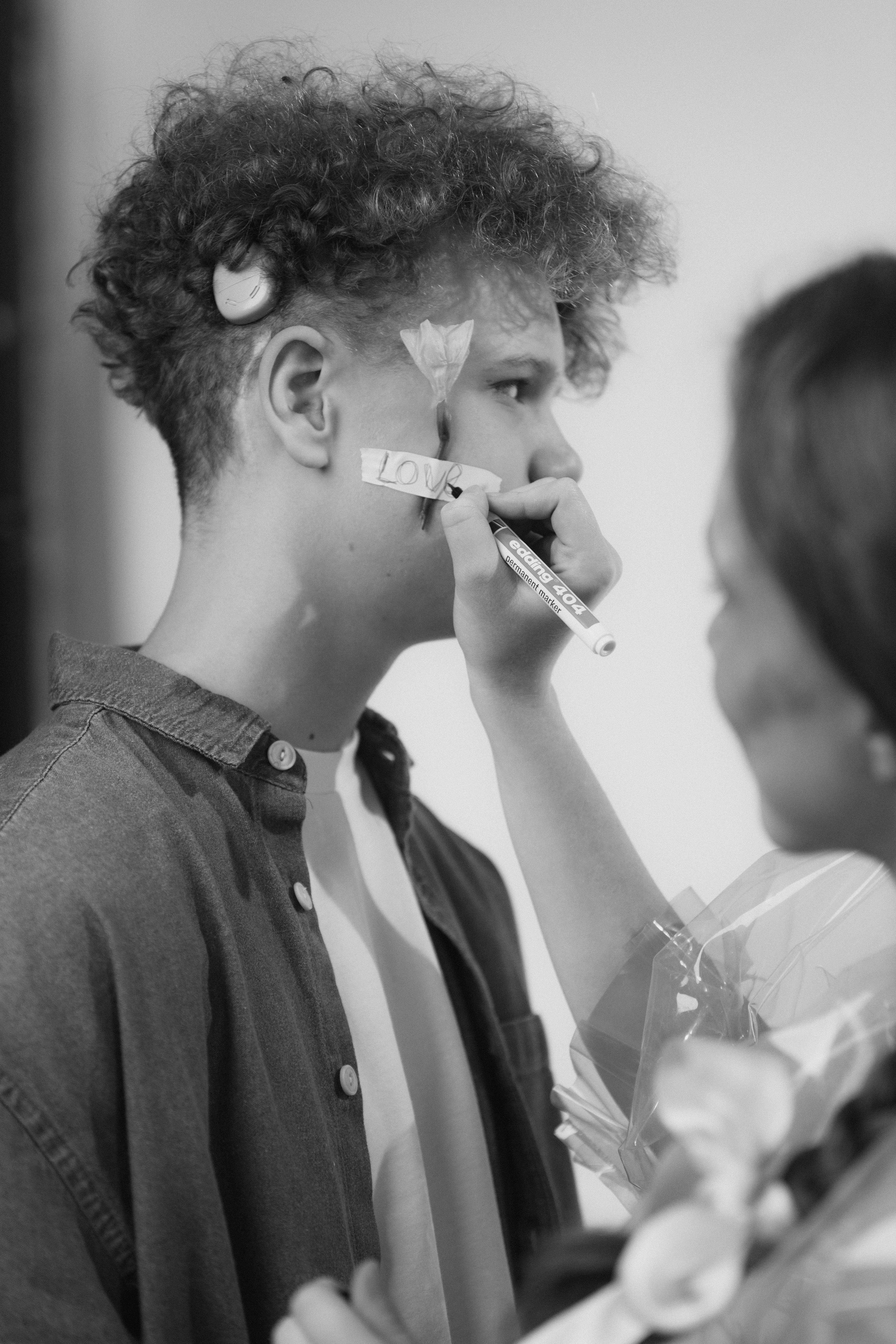 grayscale photo of a woman writing on a tape on a man s cheek