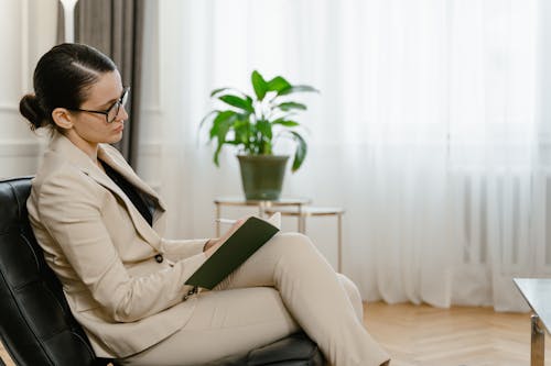 Woman Sitting on Black Leather Couch While Writing on a Notebook 