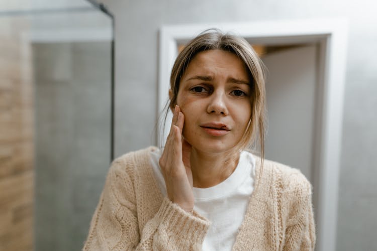 A Woman In Beige Sweater Touching Her Bruised Face