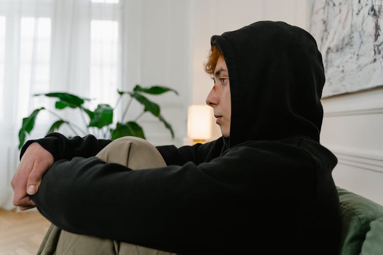 A Person In Black Hoodie Hugging His Knees While Sitting 