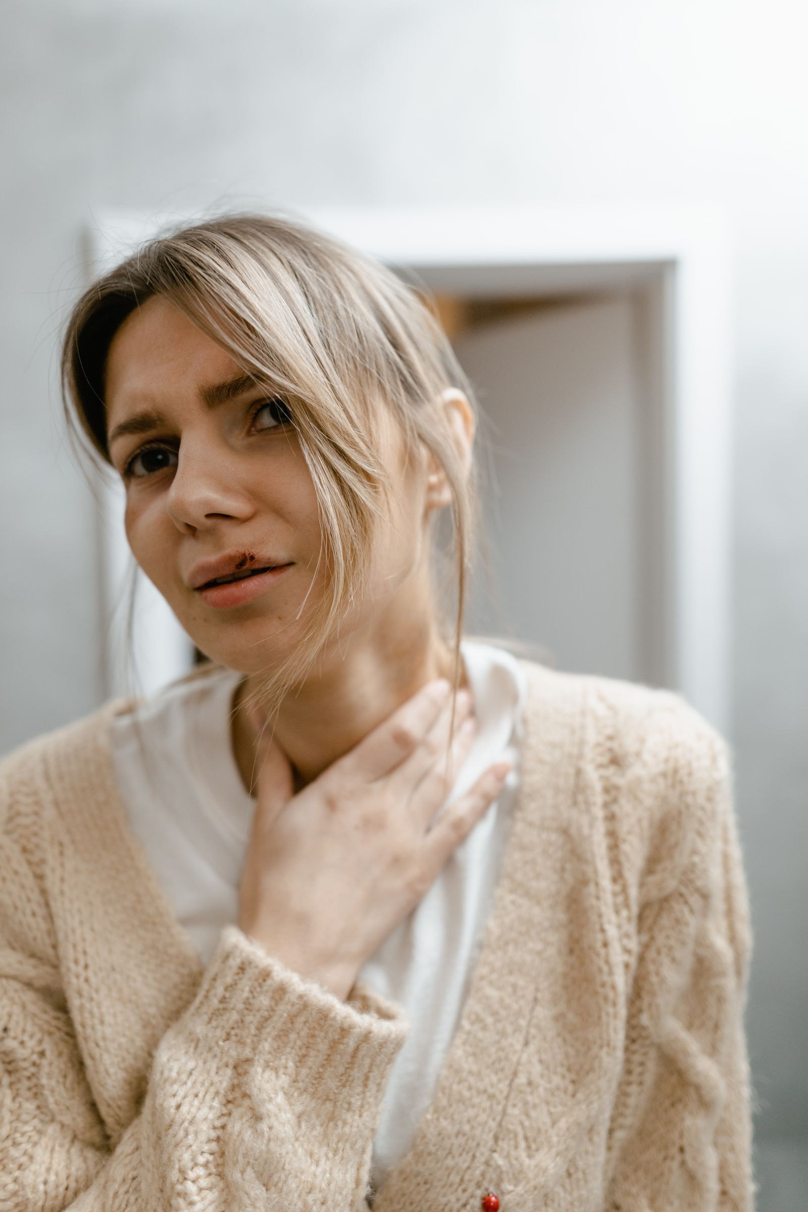A woman resting one hand at the base of her throat with a pained expression, the classic gesture of heartburn behind the breastbone