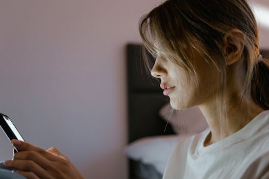Profile of a young woman attentively using her smartphone indoors, lit by screen light.