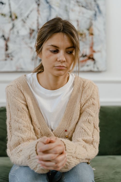 Free Contemplative young woman sitting on a couch at home, wearing a cozy sweater. Stock Photo