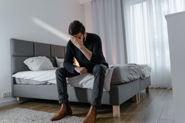 A Man In Black Sweater Sitting On The Bed