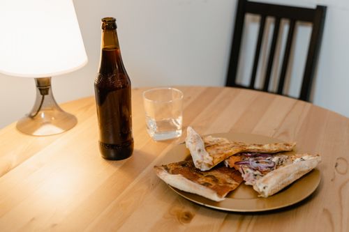 Free Warm, inviting scene featuring pizza, a beer bottle, and a soft-lit lamp on a wooden table. Stock Photo