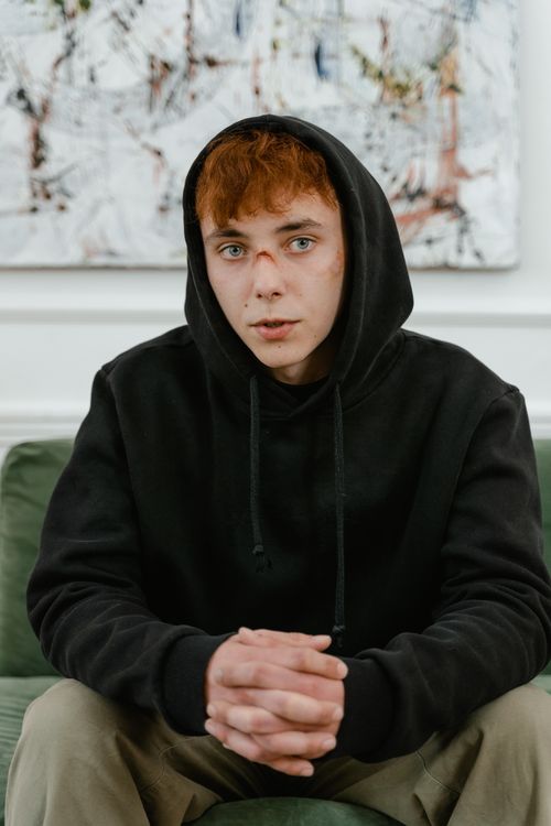 Free A young man in a black hoodie sitting indoors, appearing contemplative. Stock Photo