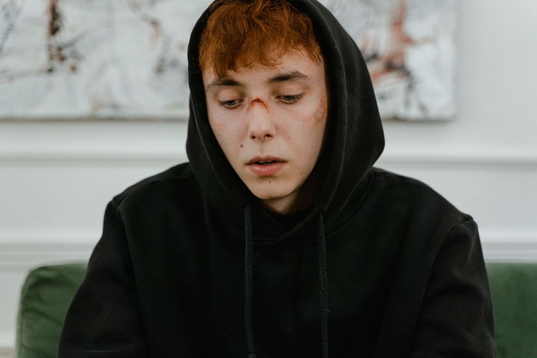A young man in a black hoodie looks contemplative and pensive indoors.