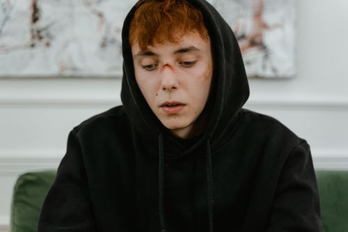 Free A young man in a black hoodie looks contemplative and pensive indoors. Stock Photo