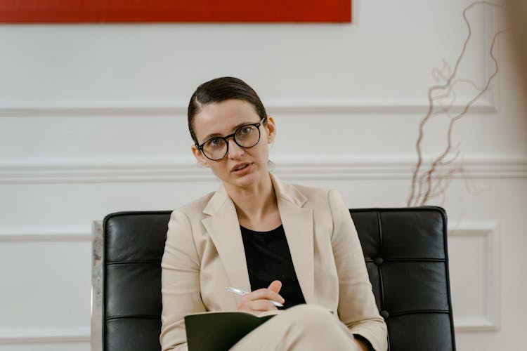 A Woman Wearing Beige Blazer Sitting On A Black Leather Chair