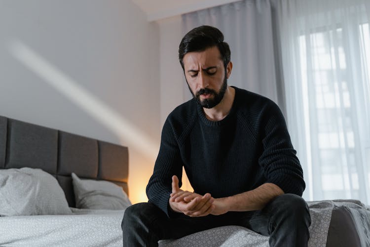 Man In Black Sweater Sitting On Bedside