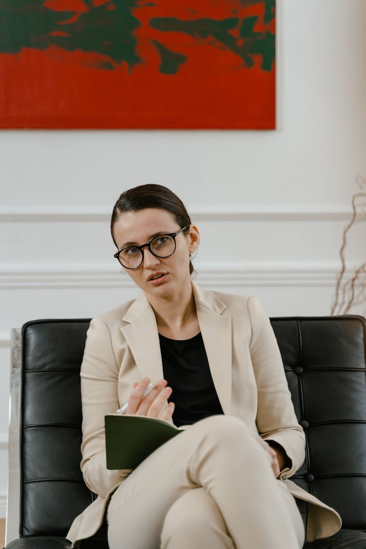 A Woman Wearing Beige Blazer Sitting On A Leather Chair