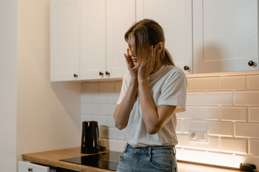 A distressed woman standing in a kitchen with her hands to her face
