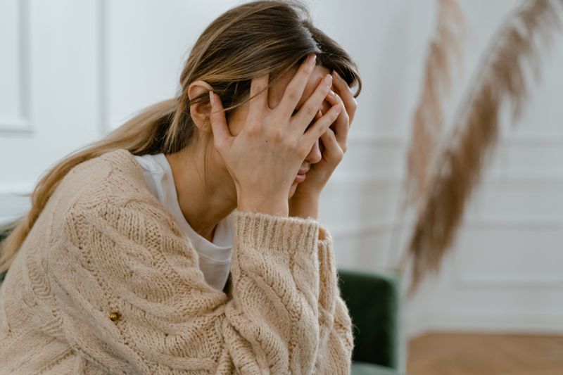 Woman sitting indoors covering her face showing stress and anxiety mental health challenges