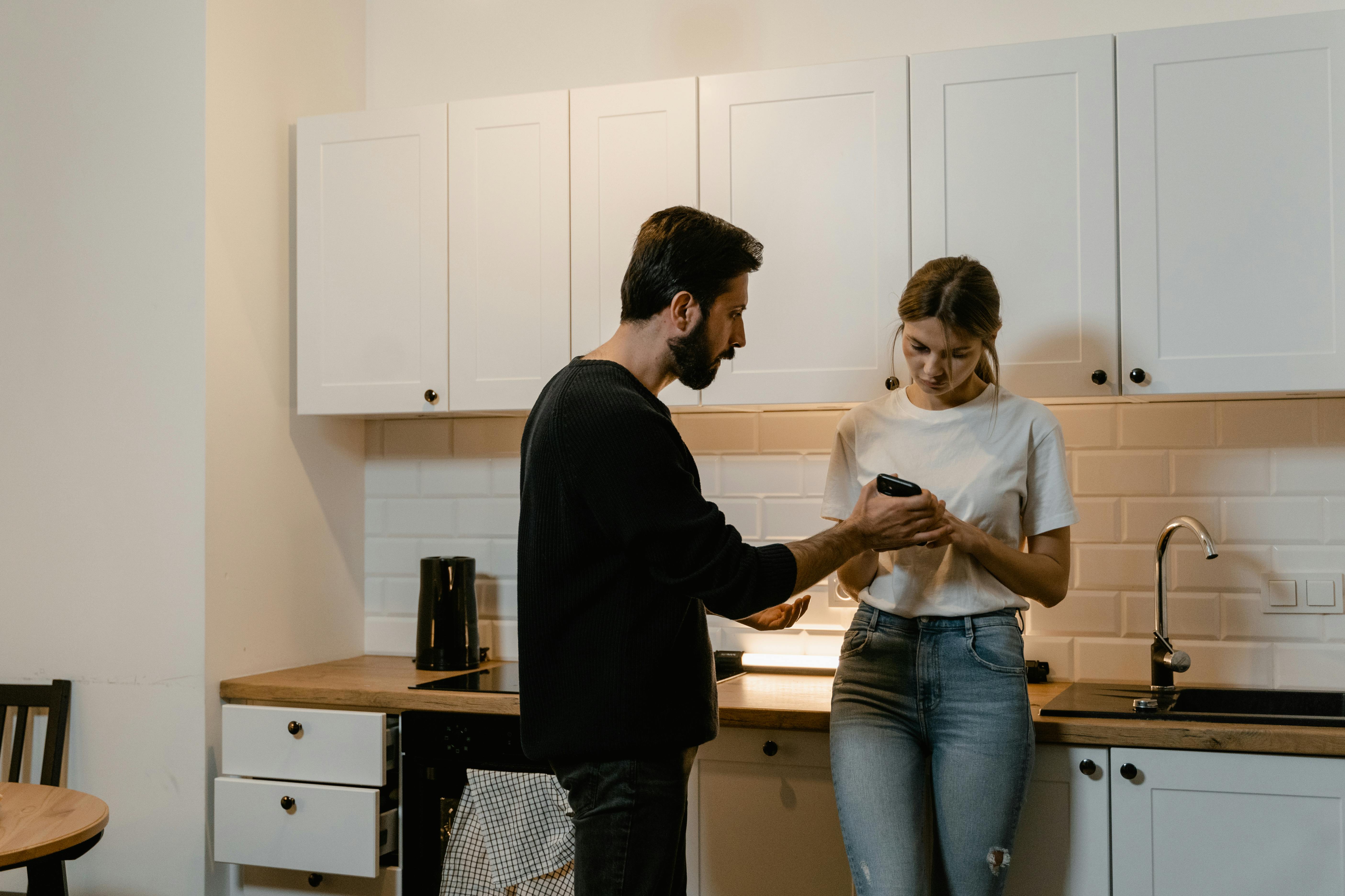 A young couple engages in a tense discussion in a modern kitchen setting.