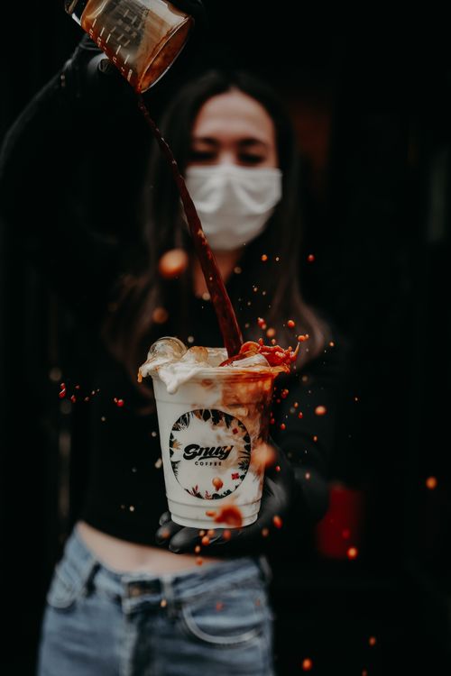 Free A masked woman pours coffee creating dynamic splash effect in a cup. Stock Photo