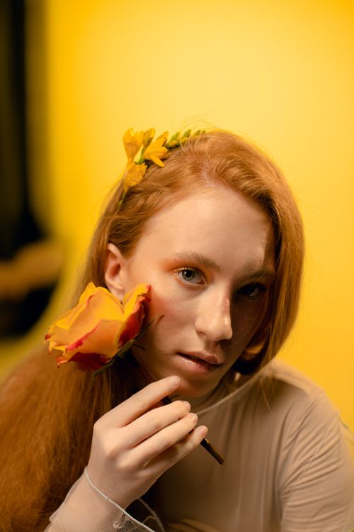 Free Close-up portrait of a woman with red hair holding yellow flowers against a warm background. Stock Photo