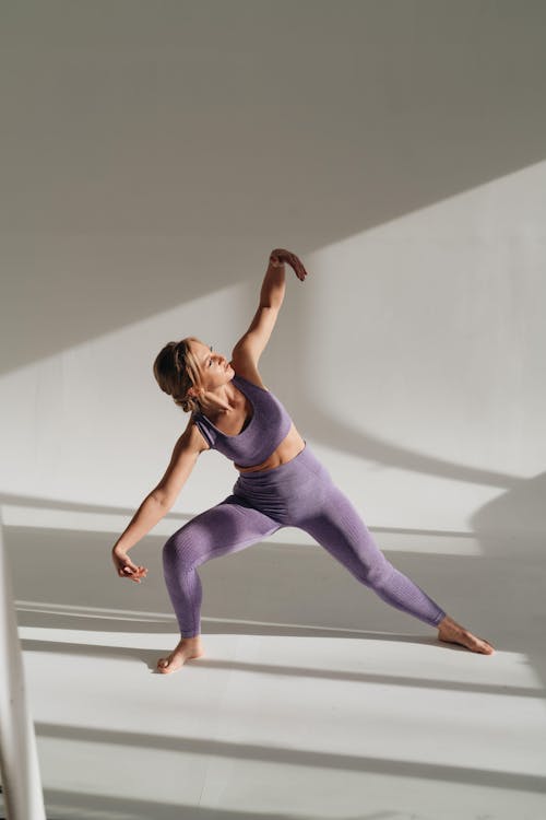 Free Full body of slim barefoot female in sportswear performing Parshvakonasana posture while practicing yoga in light studio during training on white background Stock Photo