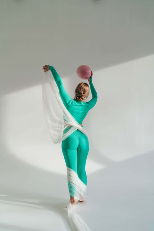 Back view of unrecognizable female in blue sportswear with silky ribbon dancing on white background
