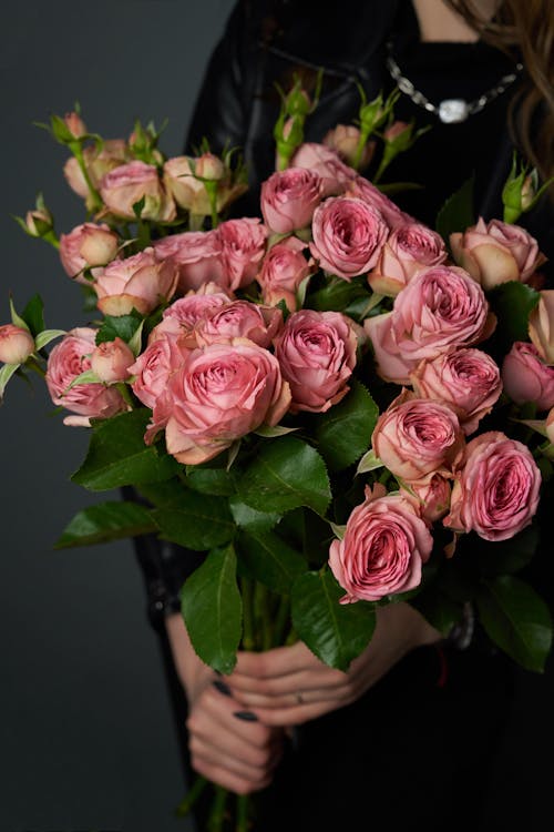 Free Crop unrecognizable female in black clothes with bunch of fresh red roses in hands against black background Stock Photo