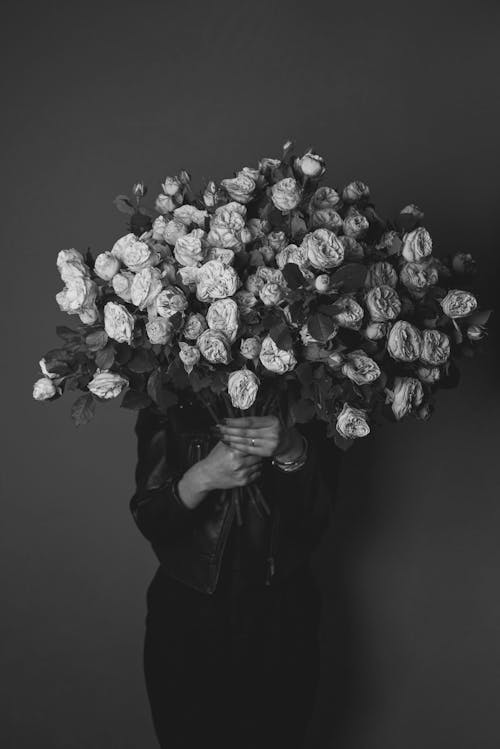 Free Black and white of anonymous female hiding face behind bunch of flowers while standing in studio Stock Photo