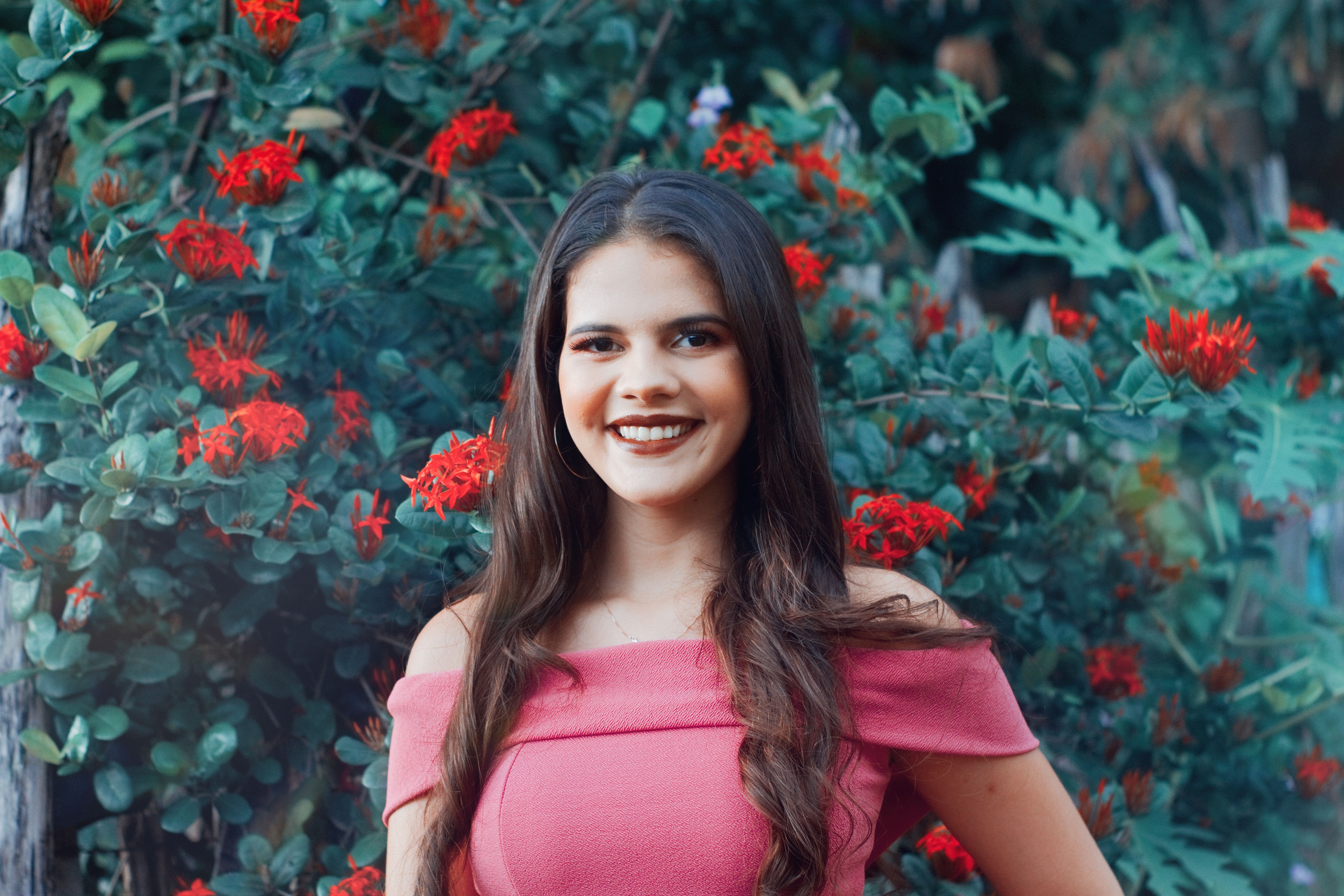Portrait of a smiling woman in pink surrounded by vibrant red flowers, exuding beauty and joy.
