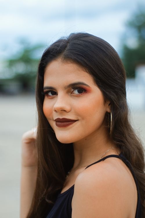 Free A captivating portrait of a woman with dark lipstick, looking back over her shoulder outdoors. Stock Photo