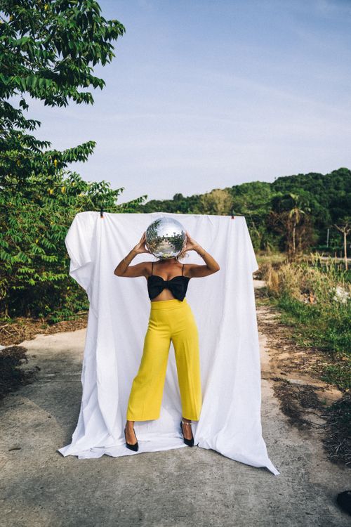 Free Fashionable woman in yellow pants holding disco ball by a sheet outdoors. Stock Photo
