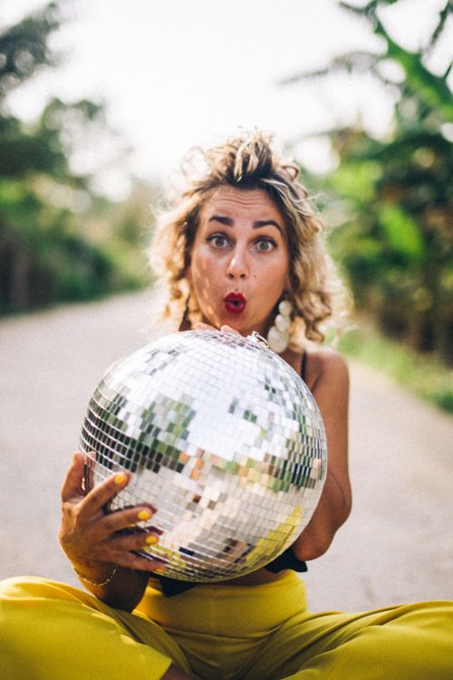 Free Joyful woman holding a disco ball outdoors with a surprised expression on a sunny day. Stock Photo