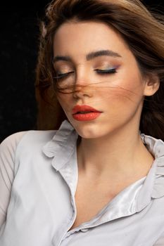 Young mindful female in gray blouse with red lips and closed eyes on black background