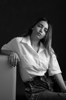 Black and white of young stylish woman leaning on hand while looking at camera with tilted head