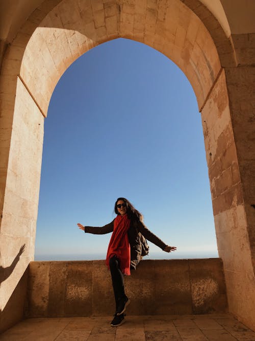 Free Woman Sitting Under Arched Opening on Clear Blue Sky Stock Photo