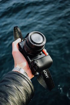 A close-up view of a hand holding a camera above a body of water, highlighting detail and perspective.