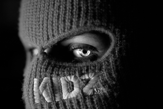 Black and white close-up photo of an eye visible through a ski mask, evoking mystery and intrigue.