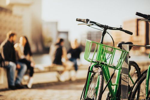 Free A green bicycle parked on an urban street with blurred people in the background. Stock Photo