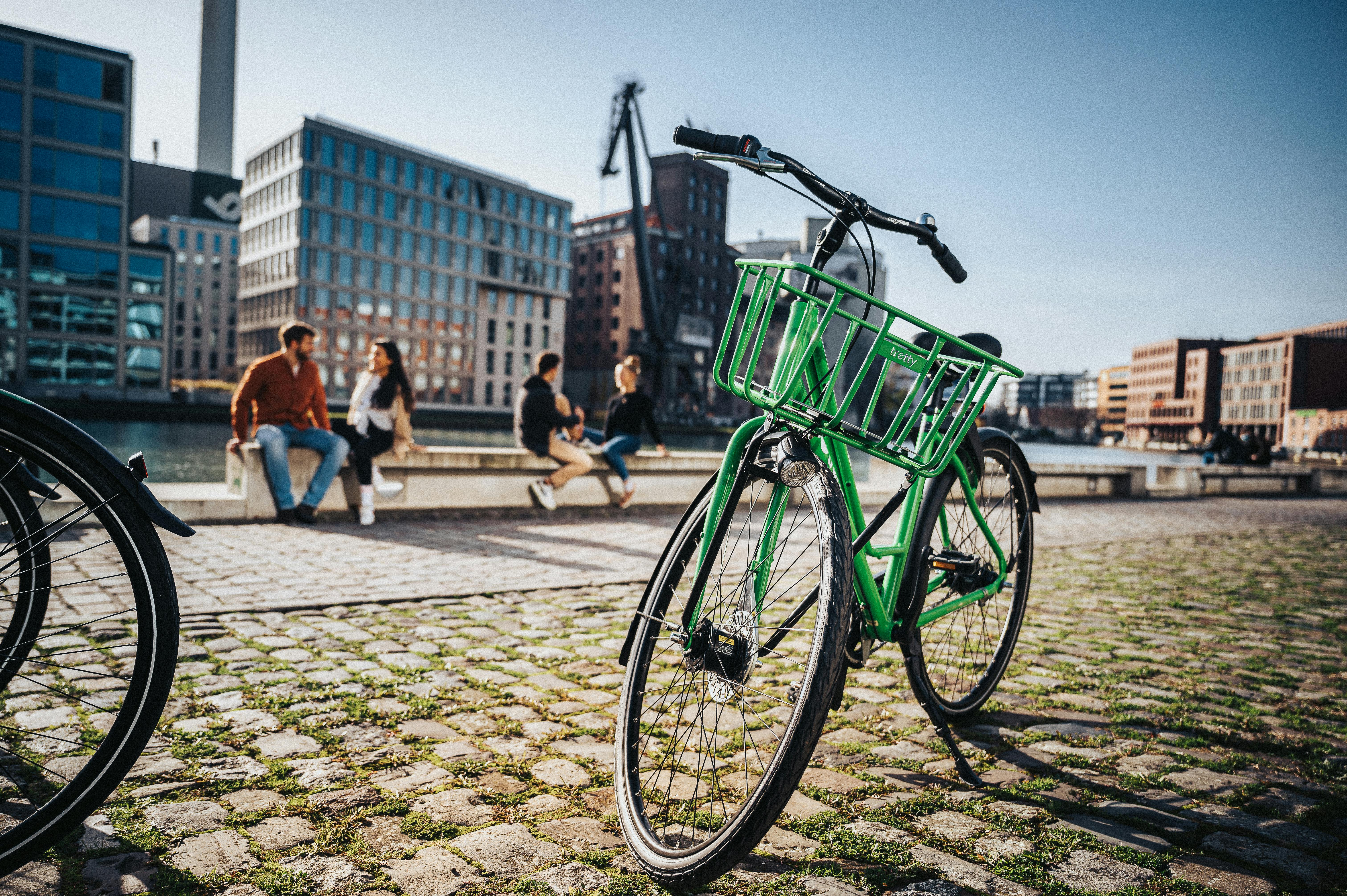 A vibrant green bicycle parked on a city street with background of modern buildings.