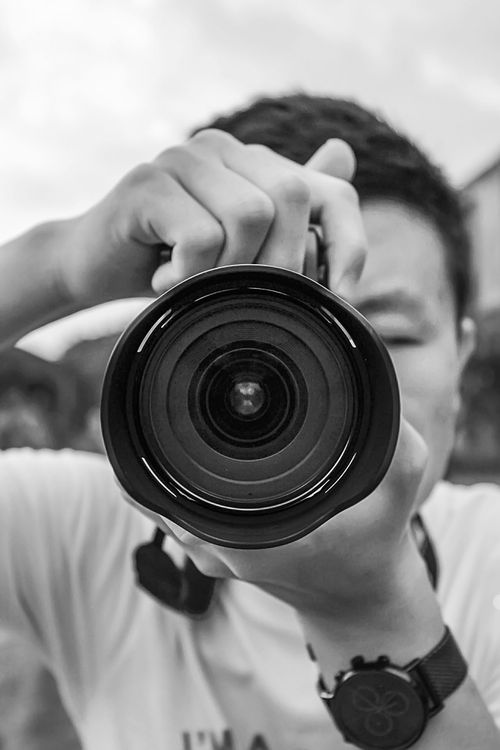 Free Close-up black and white portrait of a man holding a camera lens outdoors. Stock Photo