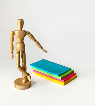 Wooden artist mannequin posed beside colorful notepads on a white surface, ideal for creative concepts.