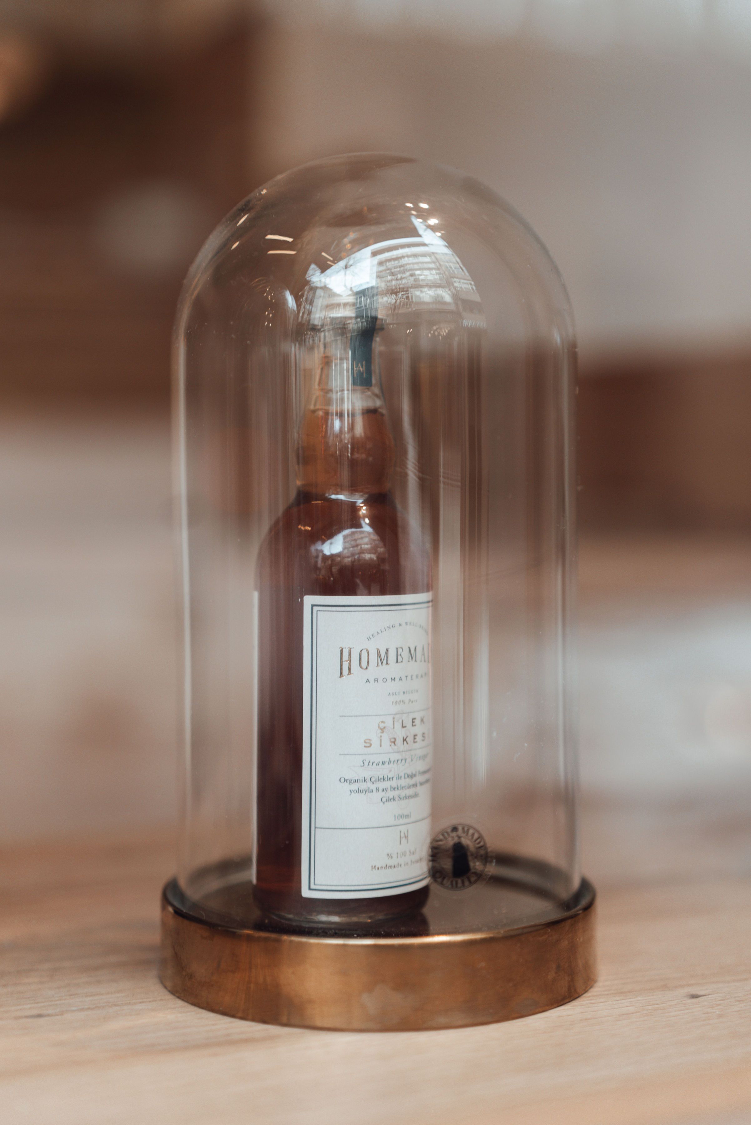 A crafted bottle encased in a glass dome displayed on a wooden surface, creating a vintage aesthetic.