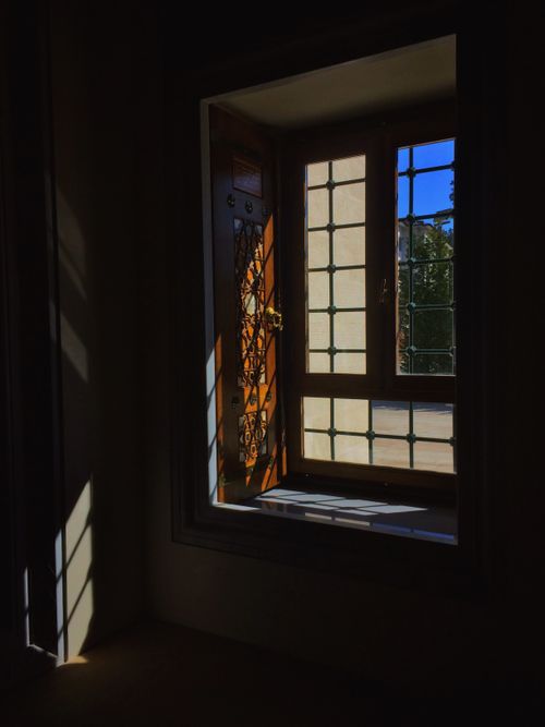 Free A dark room with sunlight streaming through a vintage wooden and glass window featuring intricate metal design. Stock Photo