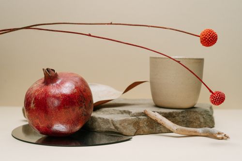 Free Elegant still life featuring a pomegranate, craspedia flowers, and ceramic mug on a stone slab. Stock Photo