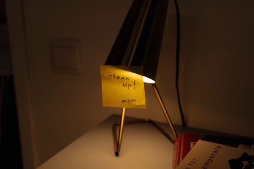 A desk lamp illuminates a sticky note with a 'clean up' reminder in warm, cozy lighting.