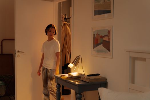 A person with short hair stands indoors next to a lit table in a cozy room.
