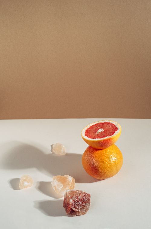 Free Elegant still life of a sliced grapefruit balanced atop another with scattered crystals on a minimalist backdrop. Stock Photo