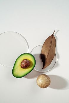 Creative composition featuring a sliced avocado, leaf, and wooden sphere on a white surface.