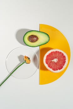 Artistic flatlay of avocado, grapefruit, and a flower on a yellow backdrop.